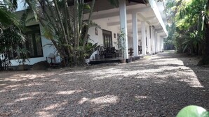 A covered outdoor area with a gravel path leading to a building with a white facade and columns. - Sea Front Hikkaduwa (Hikkaduwa)