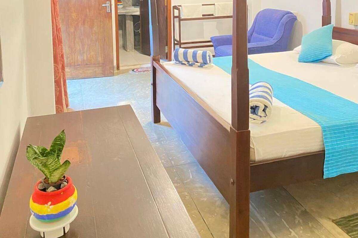 A four-poster bed with a blue and white striped pillow, a wooden nightstand with a plant, and a ceiling fan.