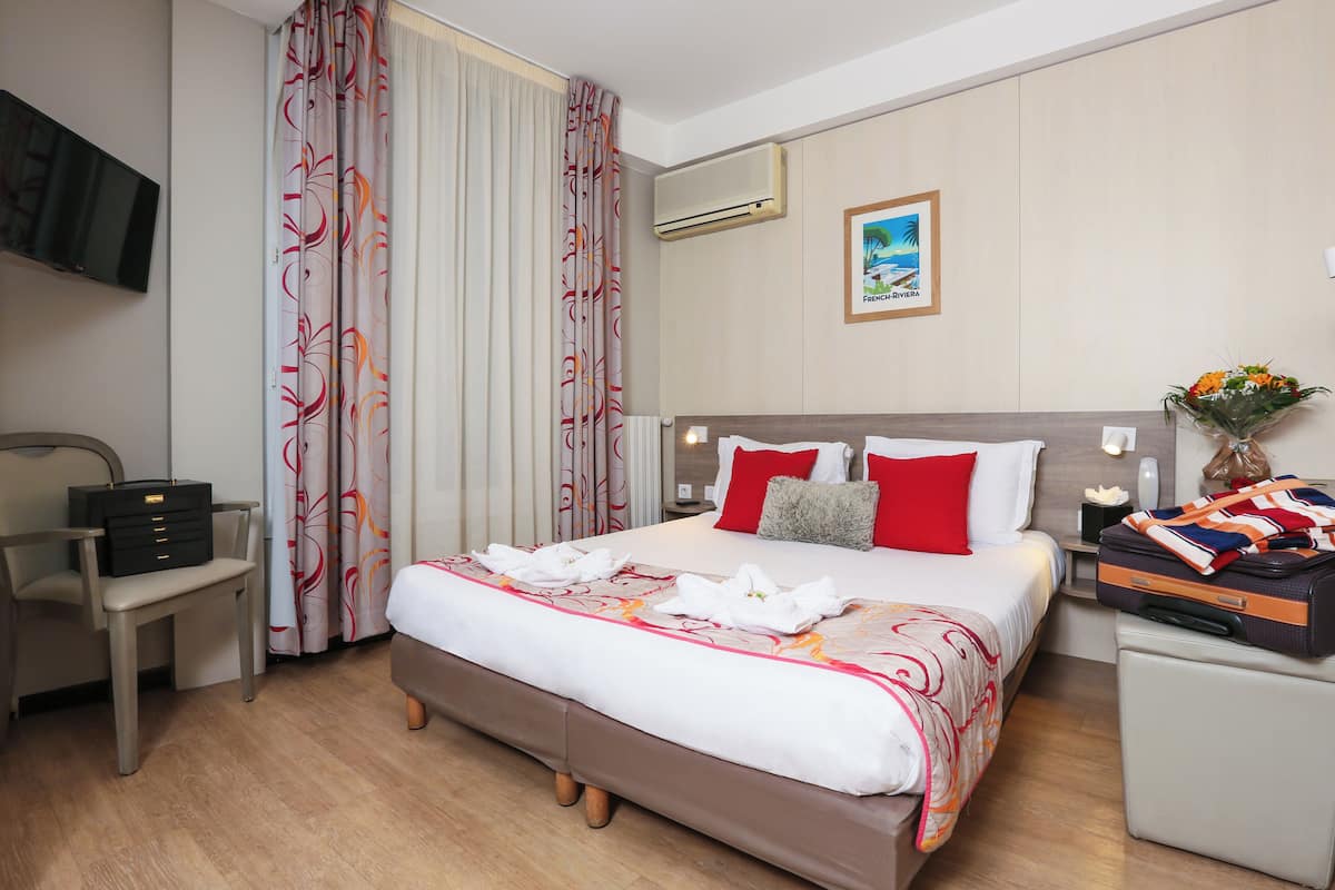 Ein Hotelzimmer mit einem großen Bett, einem Schreibtisch, einem Stuhl, einem Fernseher und einer Klimaanlage.