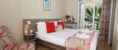 A hotel room with a bed, two bedside tables, a nightstand, a window with curtains, and a view of greenery outside.