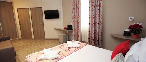 A hotel room with a bed, a TV mounted on the wall, a desk with a chair, and a small potted plant.