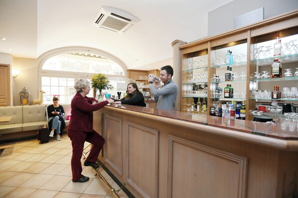 Zona de bar con mostrador, estanterías llenas de botellas y un área de estar con un sofá y una persona sentada.