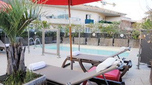 Un área junto a la piscina con sillas de descanso y una sombrilla roja.