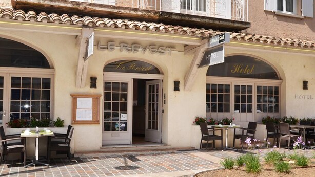 Un hotel con fachada clásica, mesas al aire libre y un letrero que indica que es un hotel.