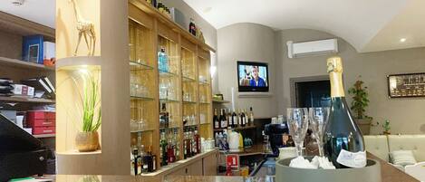 Zona de bar con encimera de mármol, un televisor en la pared y una variedad de botellas y vasos en estantes.