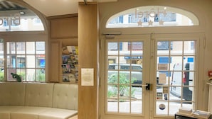 Un área de recepción con zona de estar, una columna de madera, un vidrio y vista a la calle.