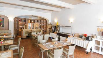 A restaurant with a cozy interior, featuring wooden furniture, a central seating area, and a kitchen visible in the background.