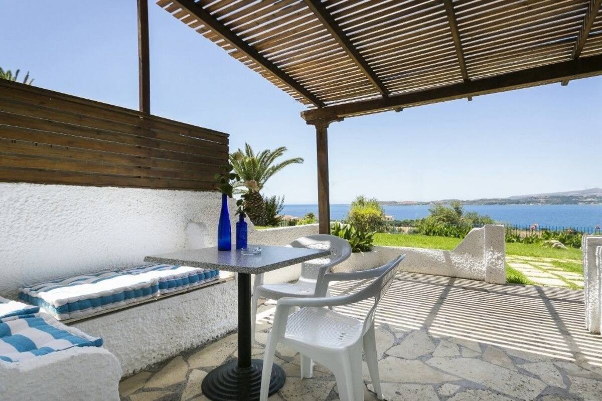 An outdoor seating area with a table and chairs, a view of the sea, and a wooden pergola.