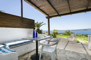 An outdoor seating area with a table and chairs, a view of the sea, and a wooden pergola.