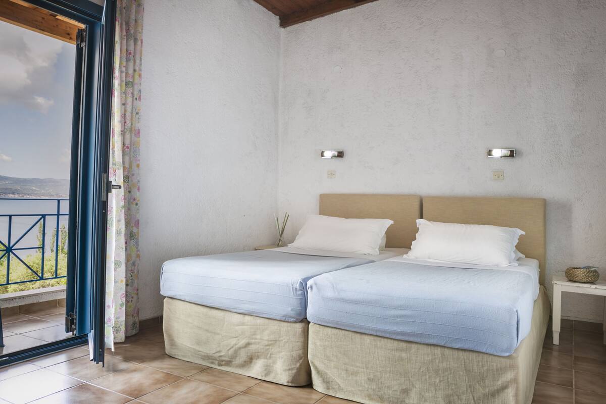 A bedroom with two beds, a window with a view, and a small bedside table.