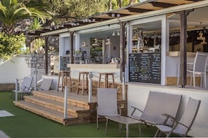 An outdoor seating area with wooden steps leading to a bar, surrounded by chairs and a menu board. - Metaxatos Apartments (Kefalonia)
