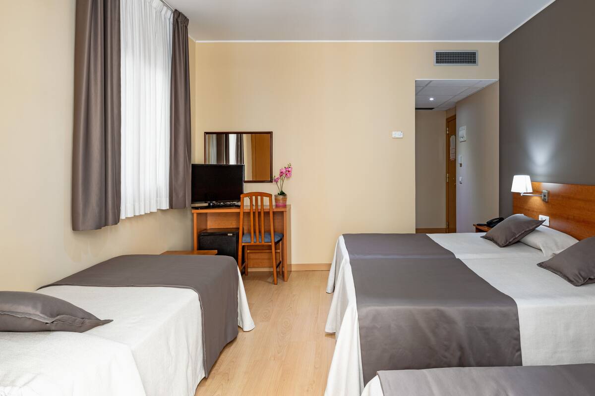 A hotel room with two beds, a desk with a chair, a television, and a small table with a vase of flowers.