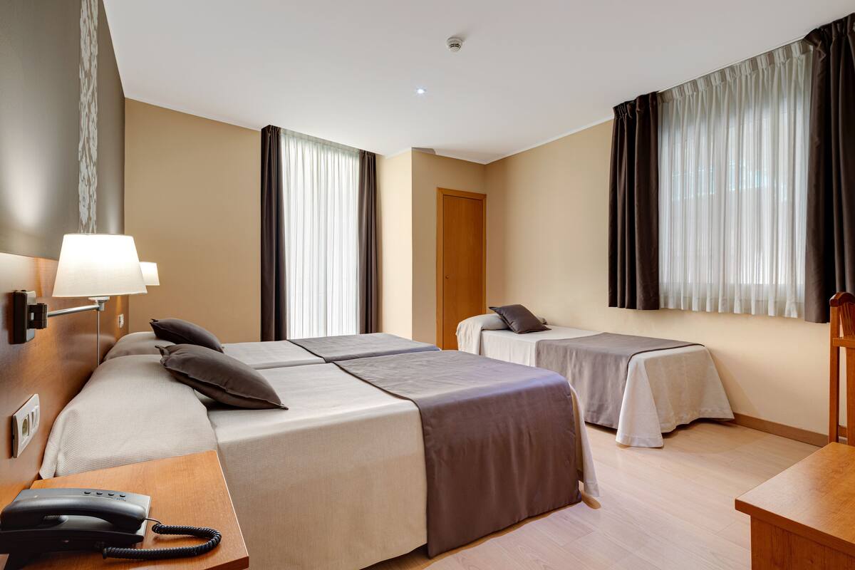 A hotel room with two beds, a desk with a telephone, and a door.