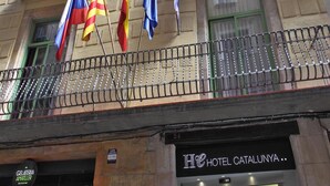 Un hotel con varios balcones, banderas y un letrero que indica que es el Hotel Catalunya.