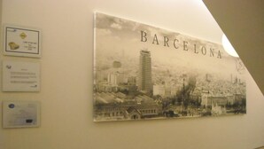 Paredes com um grande cartaz de paisagem urbana com a inscrição 'BARCELONA' e vários documentos ou certificados no lado esquerdo.