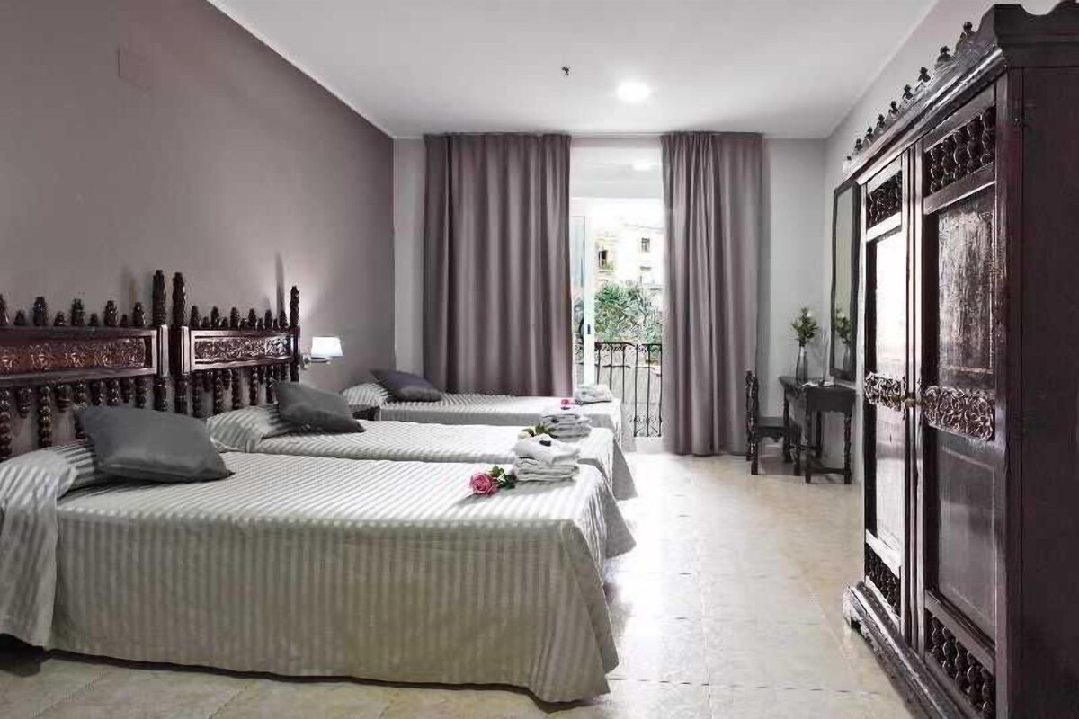 Quarto de hotel com três camas, um guarda-roupa de madeira grande e uma varanda com cortinas.