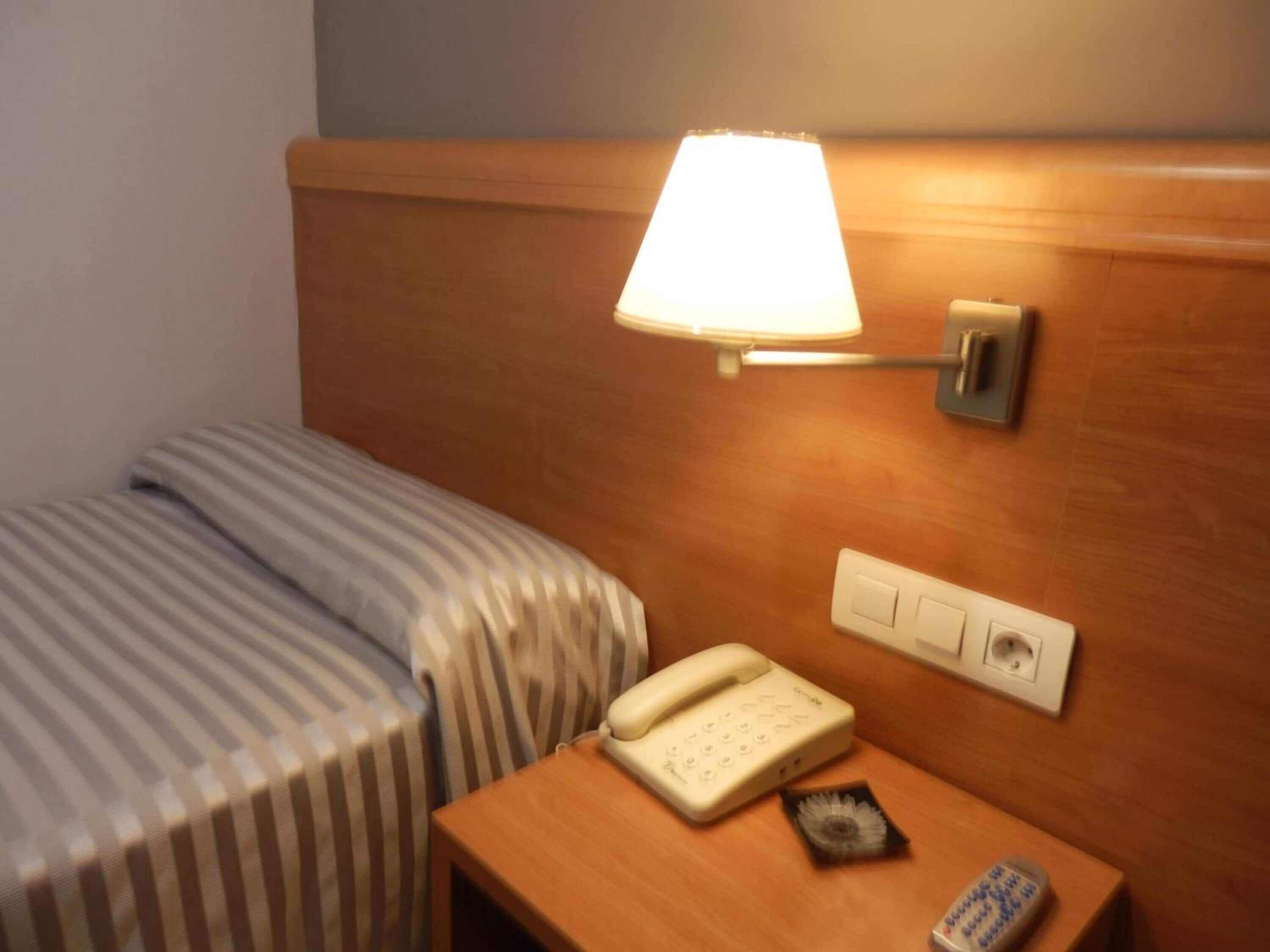 Ein Hotelzimmer mit einem Bett, einem Nachttisch mit Lampe, einem Telefon und einer Steckdose.