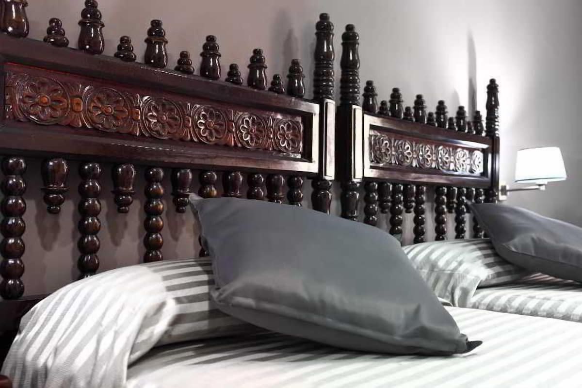 A hotel room with a large bed, a wooden headboard with intricate carvings, and a bedside lamp.