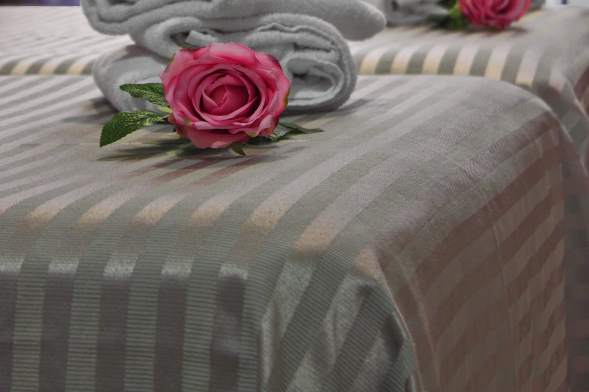 Una cama bien hecha con toallas dobladas y una rosa rosa.