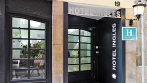 Entrada de hotel com porta de vidro, placa indicando 'HOTEL INGLES' e um poste de luz.