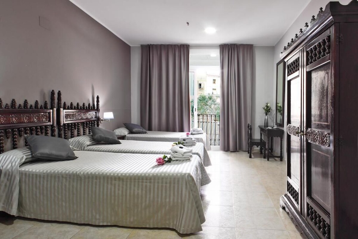 Quarto de hotel com três camas, um guarda-roupa espaçoso e vista para o exterior.