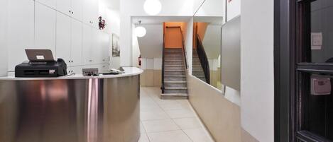 A reception area with a curved counter, a laptop, and a staircase leading to an upper floor.