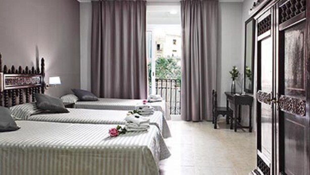Quarto de hotel com duas camas de solteiro, um espelho grande, um guarda-roupa e uma varanda com cortinas.