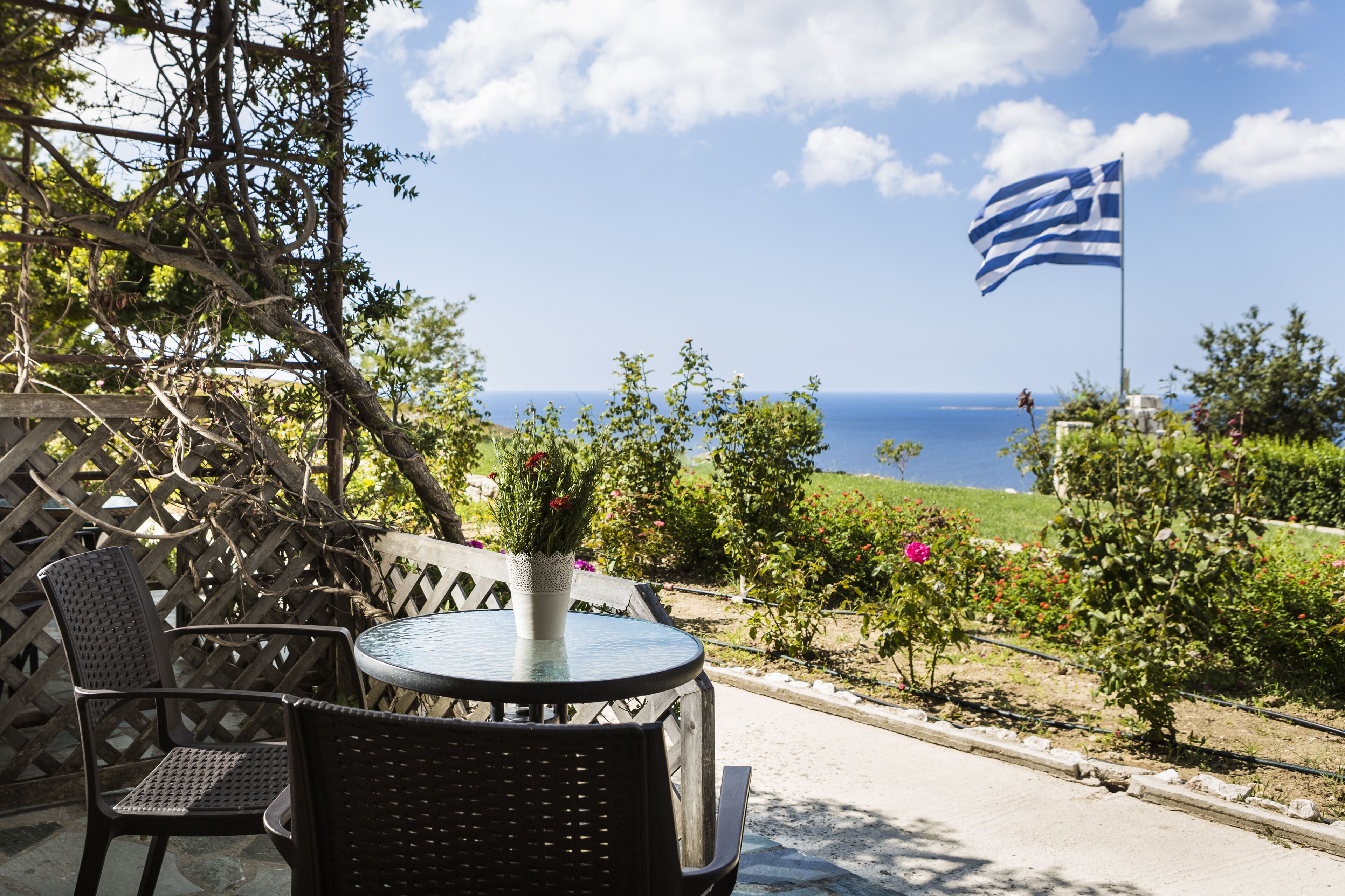 A patio with a table and chairs, a view of the sea, and a flag.