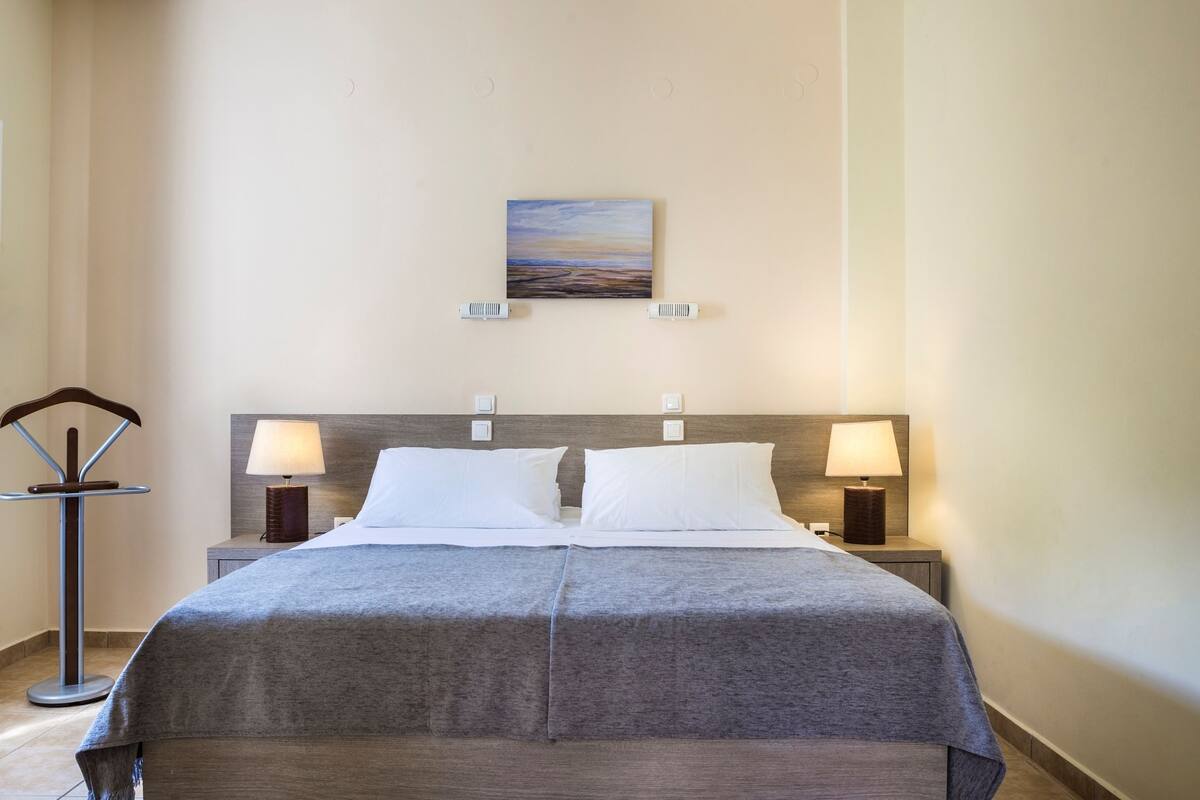 A hotel room with a large bed, two bedside lamps, a painting on the wall, and a floor lamp.