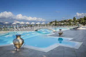 A pool area with lounge chairs and umbrellas, a decorative vase, and a view of the sea. - Dionysos Village Resort (Kefalonia)