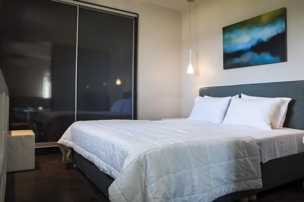A modern hotel room with a large bed, a sliding glass door, and a painting on the wall.