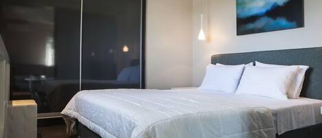 A modern hotel room with a large bed, a sliding glass door, and a painting on the wall.