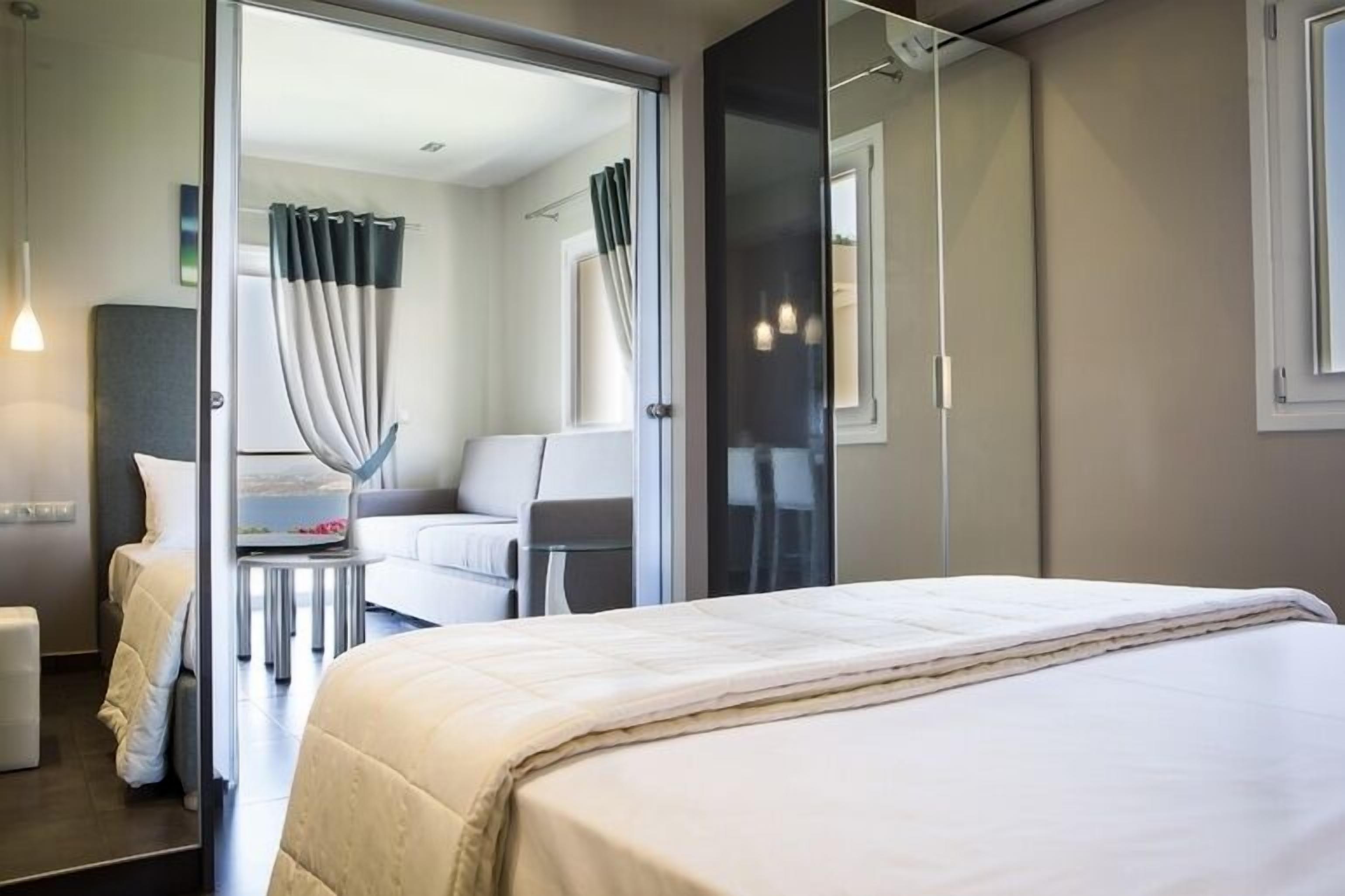 Ein modernes Hotelzimmer mit einem großen Bett, einem Schreibtisch mit Stuhl, einer Couch und einer Glastrennwand.