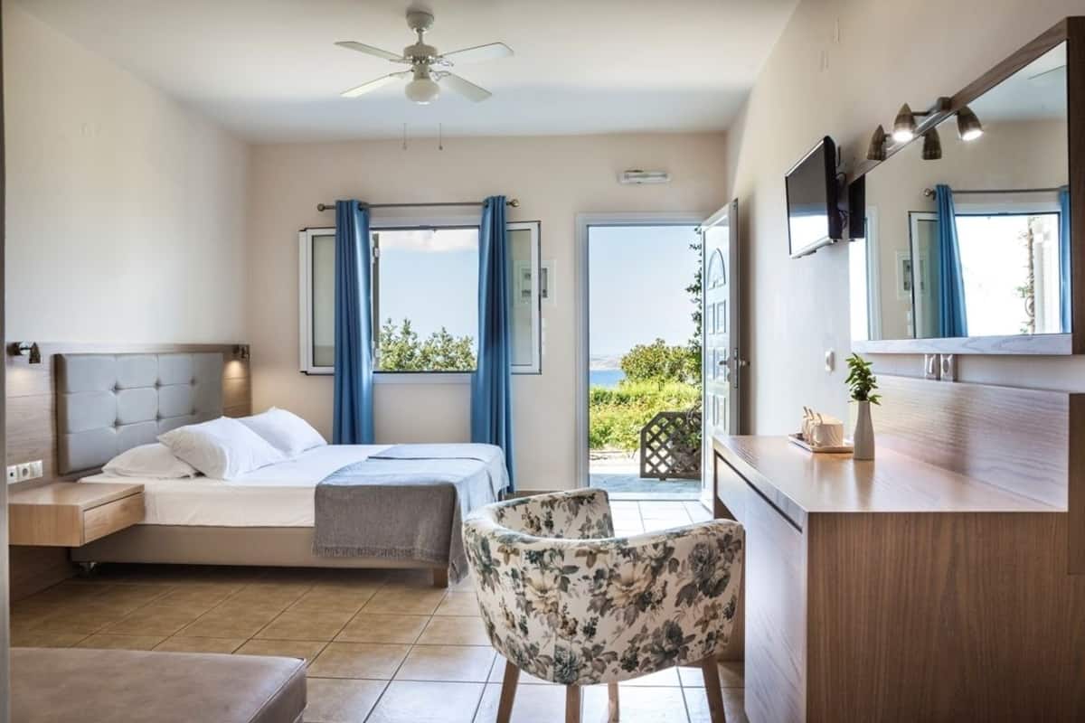 A bedroom with a bed, a chair, a desk, and a balcony with a view.