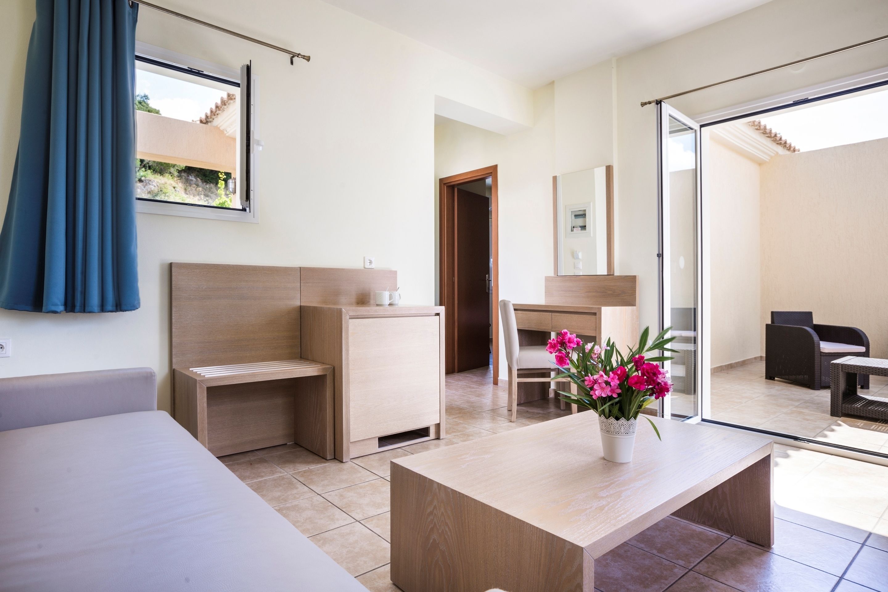 Una habitación de hotel moderna con cama, escritorio, silla y un mueble pequeño. Hay una ventana con cortinas y vistas al exterior.