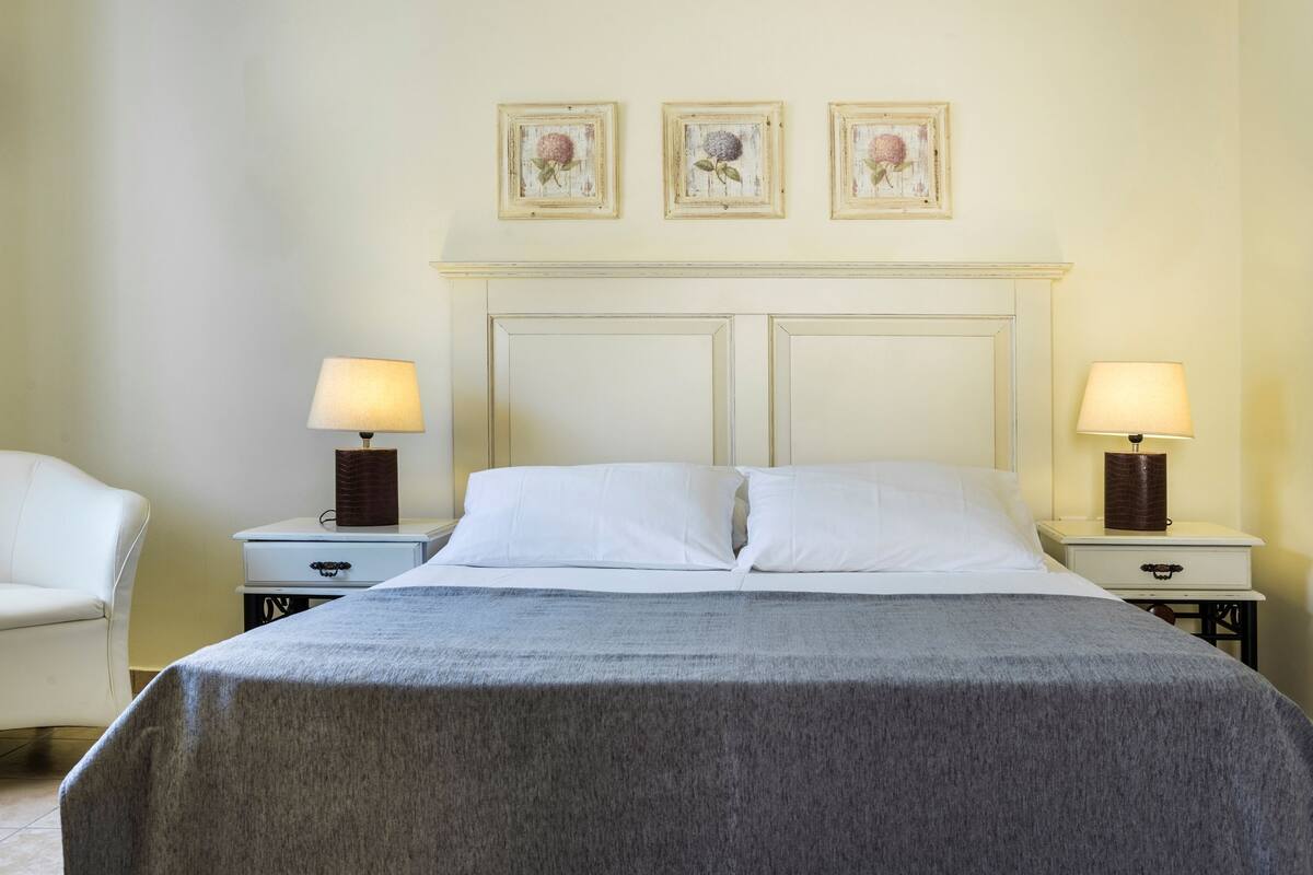 A hotel room with a bed, two bedside tables with lamps, a chair, and three framed pictures on the wall.