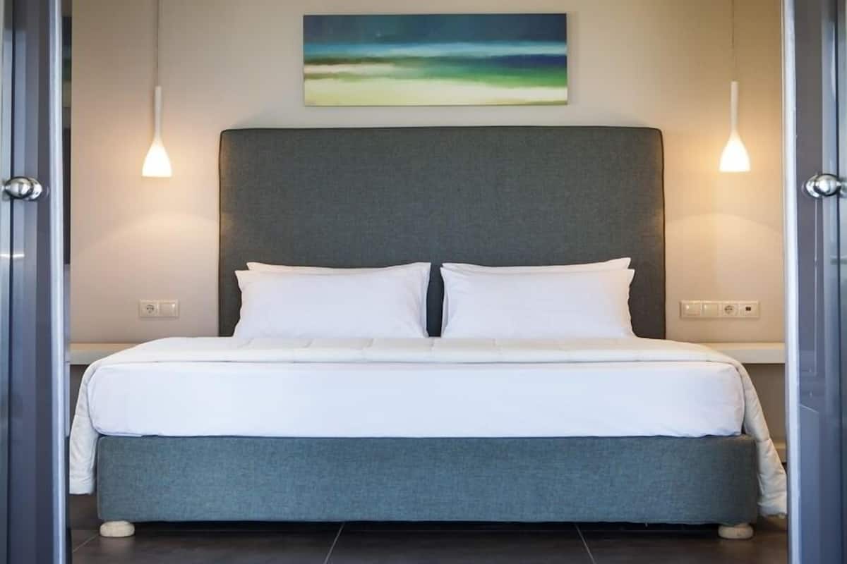 A modern bedroom with a large bed, grey upholstered headboard, white bedding, and two pendant lights.