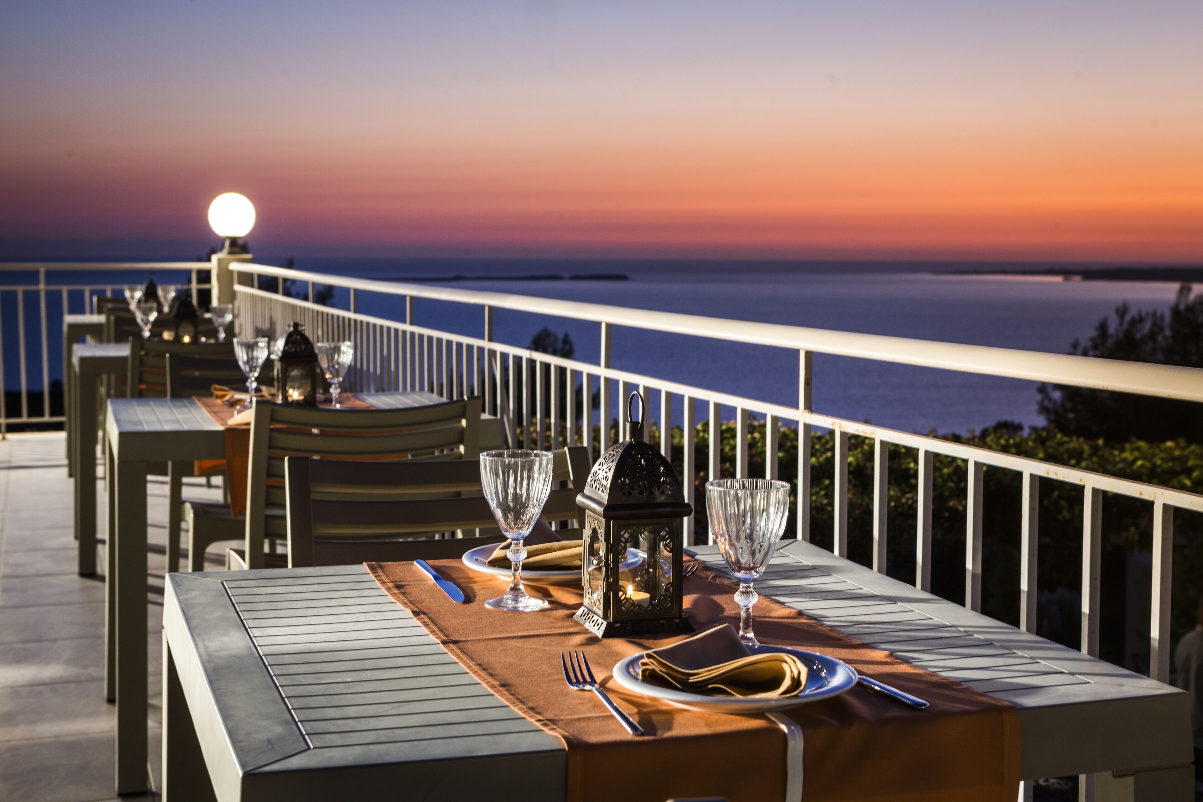 A table set for dining with a view of the ocean at sunset.