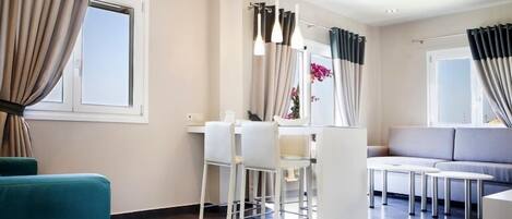 Un salon moderne comprenant un canapé, un coin repas avec des chaises et un espace cuisine avec un comptoir et des chaises.