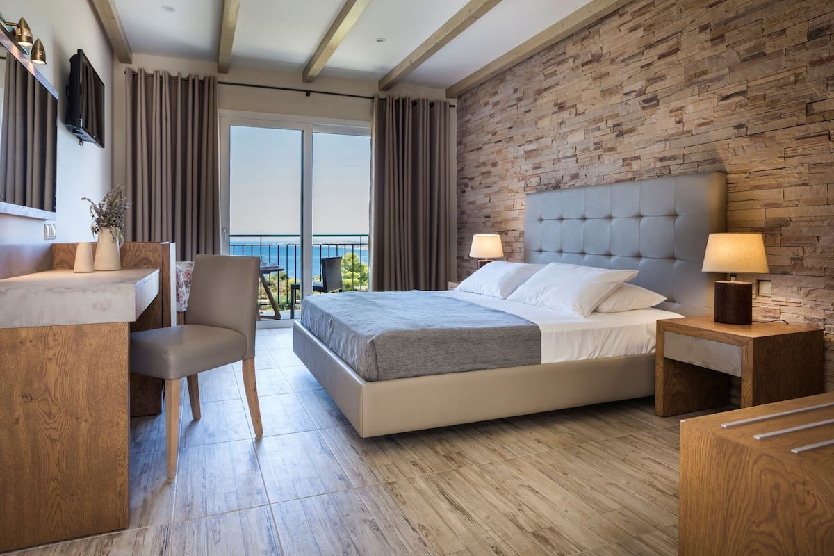 A modern hotel room with a large bed, a desk, and a chair. The room has a balcony with a view.