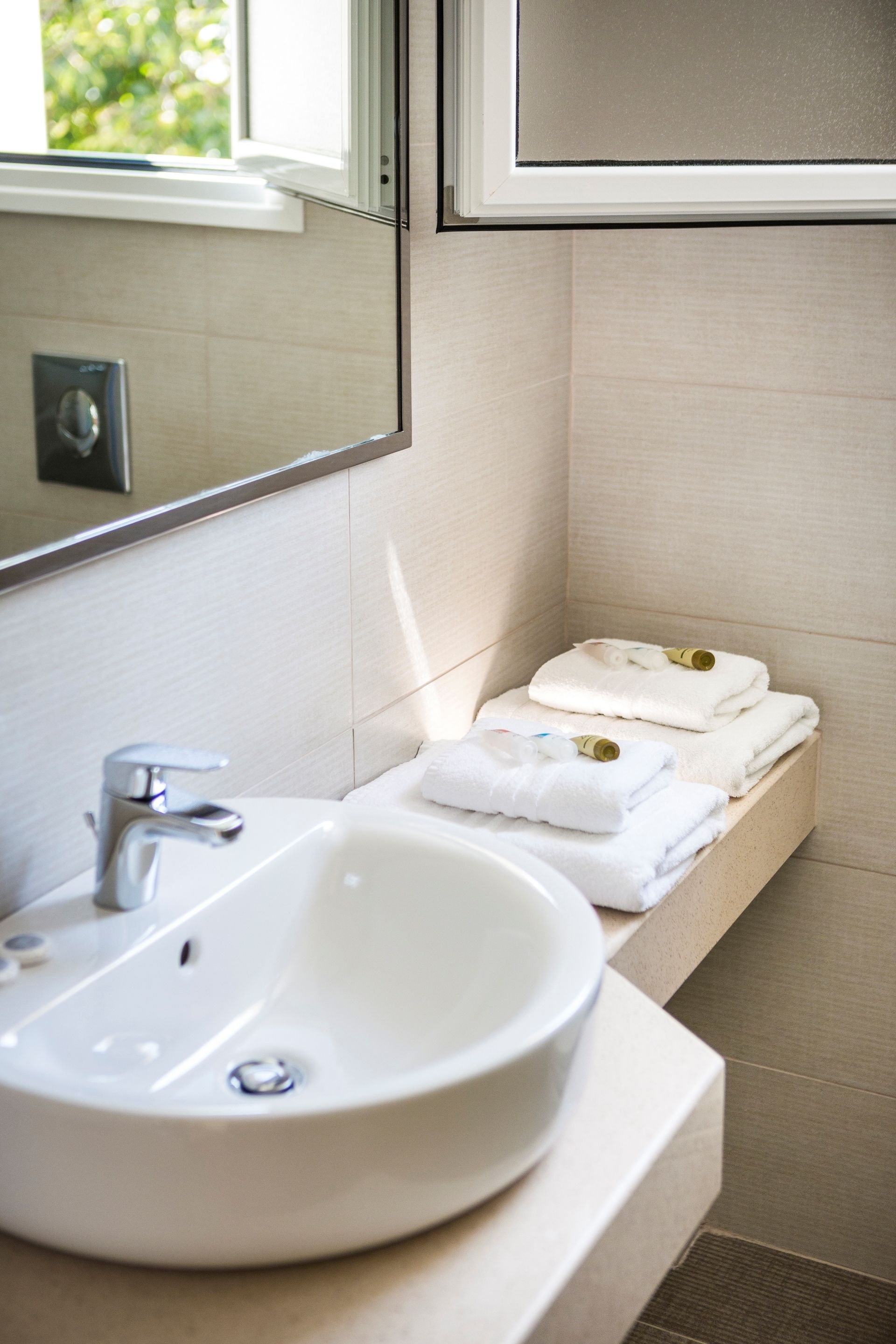 A bathroom with a white sink, a mirror, and a shelf with folded towels.