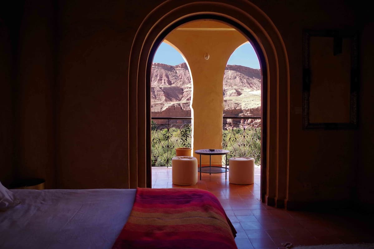 Una habitación de hotel con cama, una colcha colorida y un balcón con mesa y sillas.