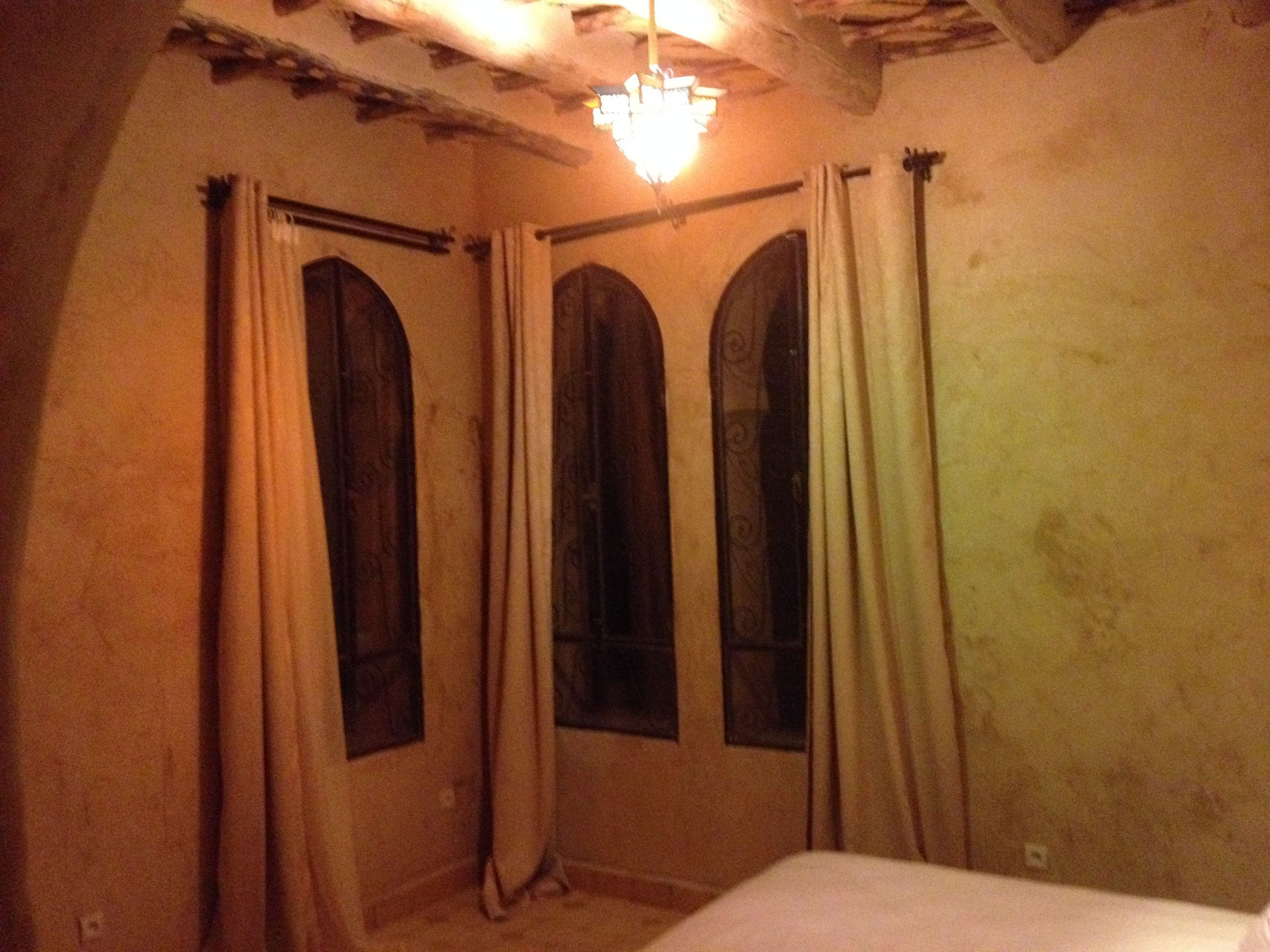 Ein Zimmer mit drei Rundbogenfenstern, einem Bett und einer Chandelüster.