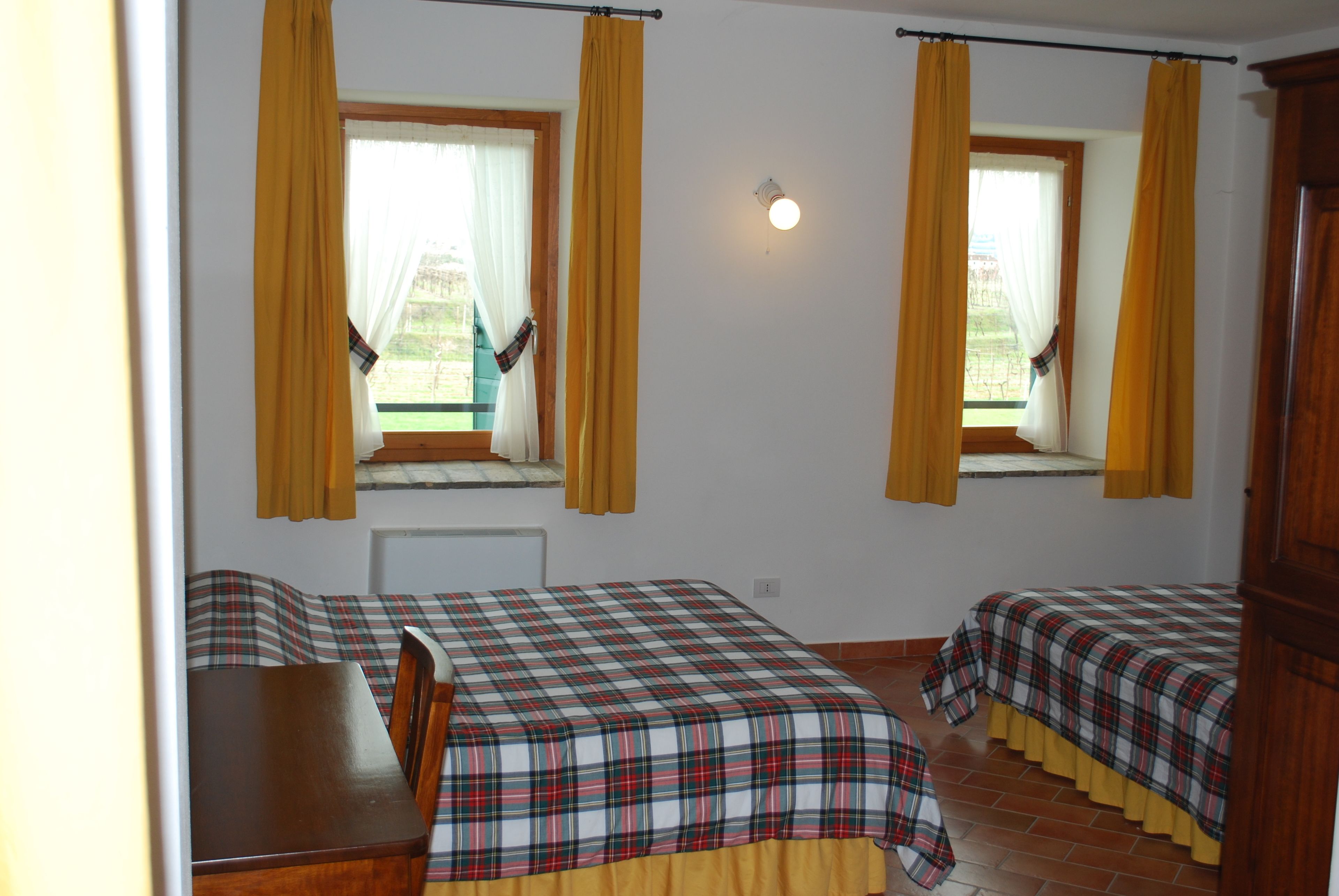 Ein Zimmer mit zwei Betten, einem Holztisch und einem Fenster mit gelben Vorhängen.