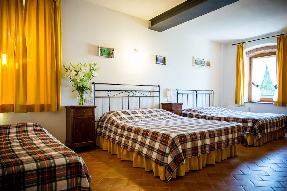A hotel room with three beds, a wooden cabinet, a vase with flowers, and a window with curtains.
