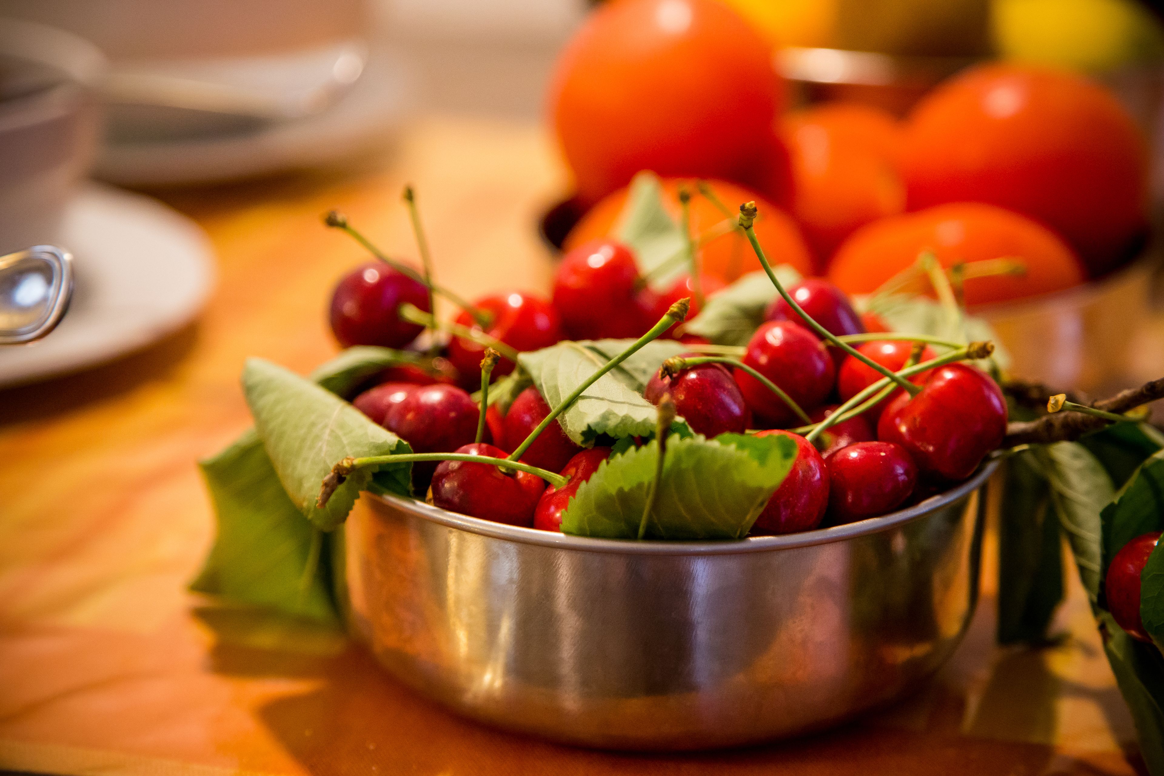 A metal bowl filled with cherries and leaves on a wooden table.