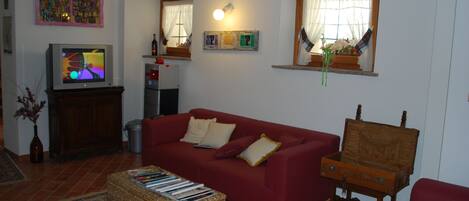 Ein Wohnzimmer mit einem roten Sofa, einem Fernseher, einer Holzkiste und einem Teppich.