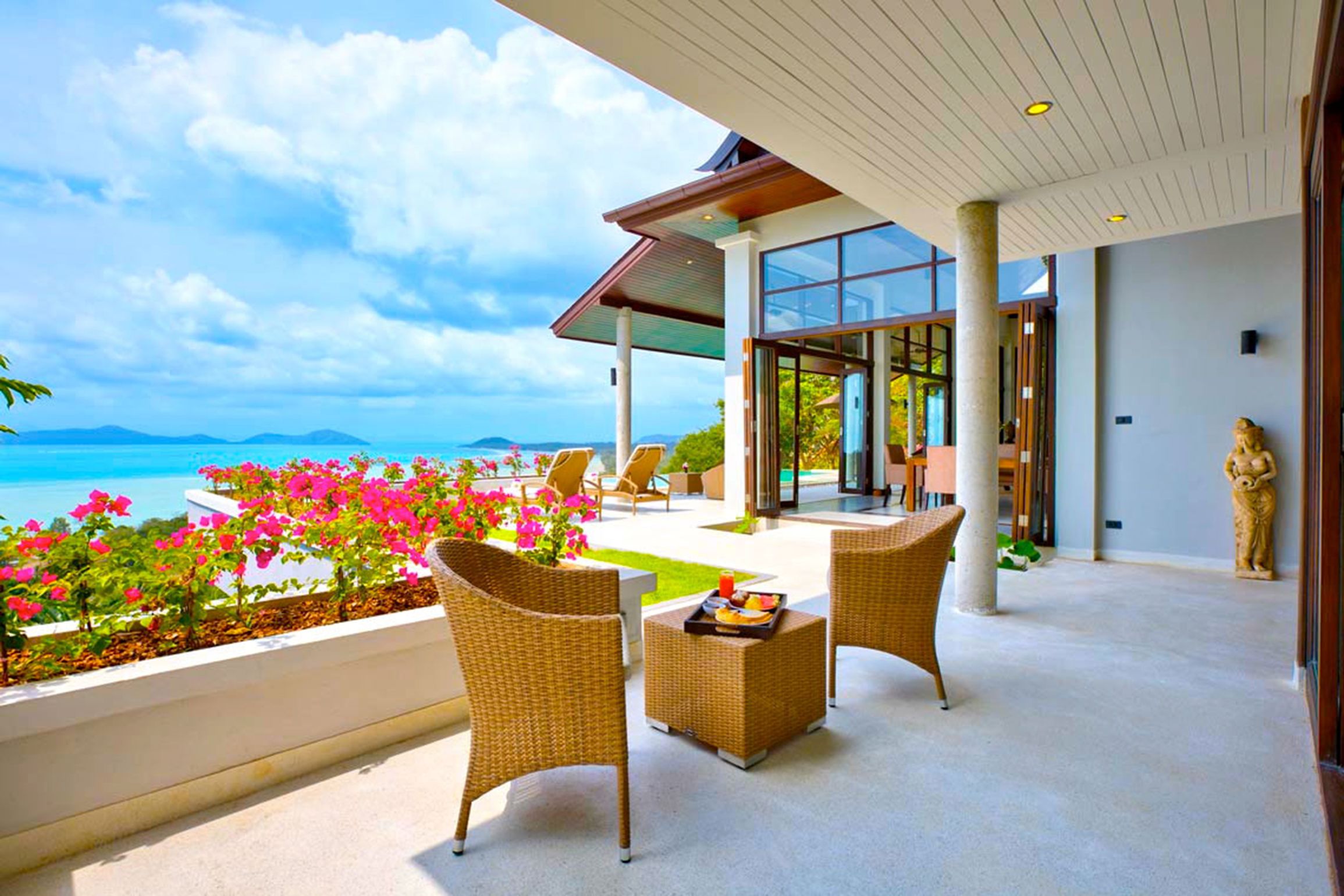 An outdoor seating area with wicker furniture, a glass enclosure, and a view of the sea.