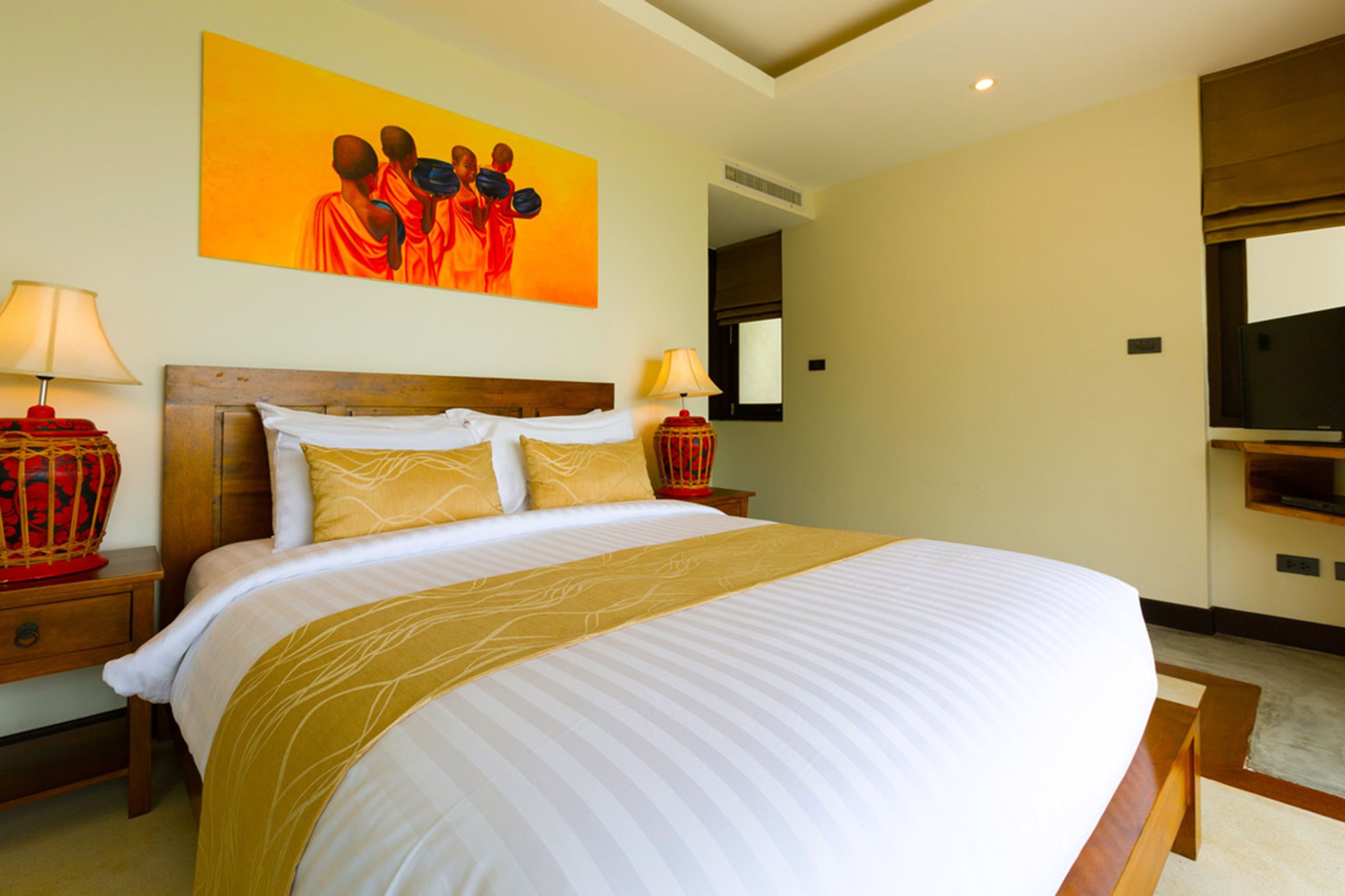 Quarto de hotel com uma cama grande, duas mesas de cabeceira com abajures, uma televisão e um quadro na parede.