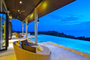 Un área lounge moderna al aire libre con vistas a una piscina grande y al océano al atardecer.
